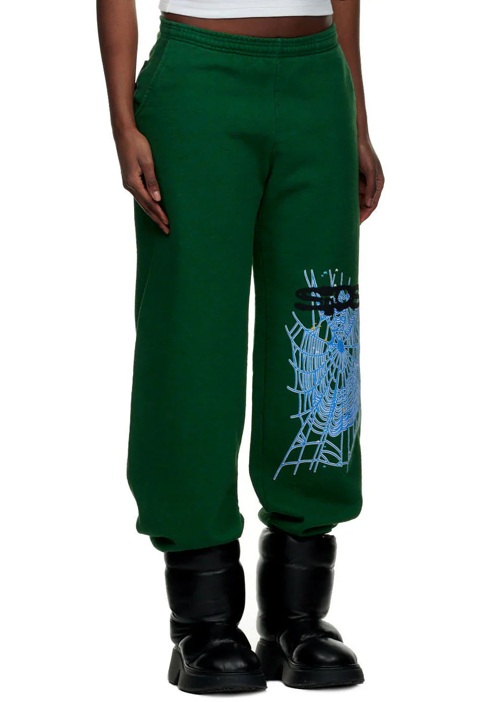 Someone styles the 100% Cotton Sp5der Sweatpants for Men—dark green streetwear joggers with a spider web graphic and relaxed fit—with black boots and a white top for a cool urban look.