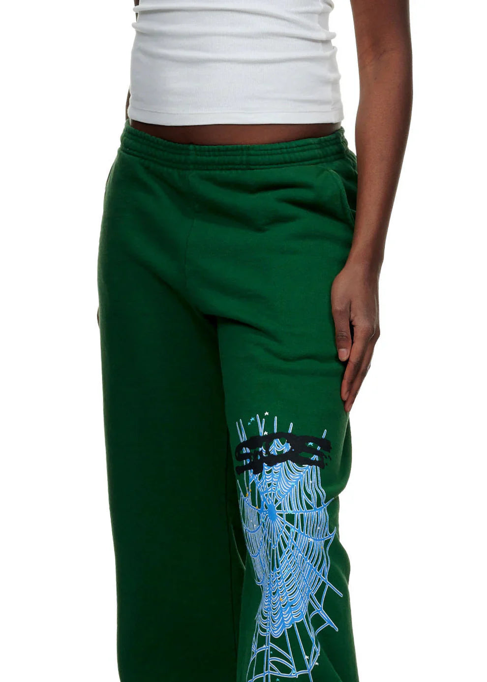 A person in a white tank top and 100% Cotton Sp5der Sweatpants for Men—dark green streetwear jogger pants with a spider web graphic and relaxed fit—stands against a white background.