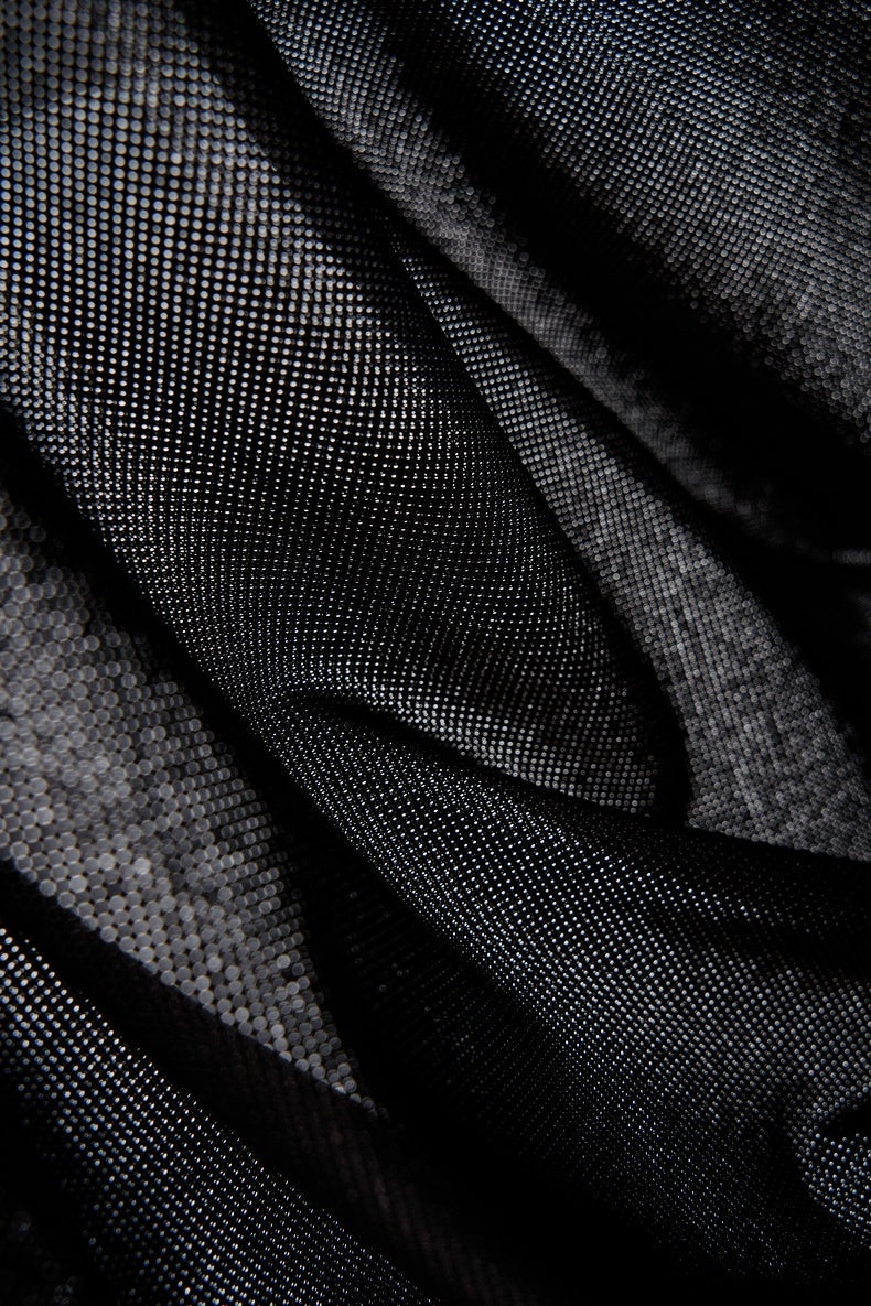 Close-up of black textured fabric with a subtle dot pattern and draped folds on a streetwear graphic tee