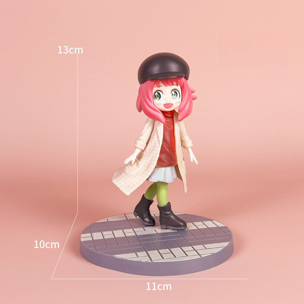 The Spy x Family Detective Anya PVC Figure Set showcases the character in her movie version, featuring iconic pink hair under a black beret, and attire of a beige coat, red shirt, and green pants. This 14 cm tall figure stands on a round tiled base measuring 10 cm by 11 cm.