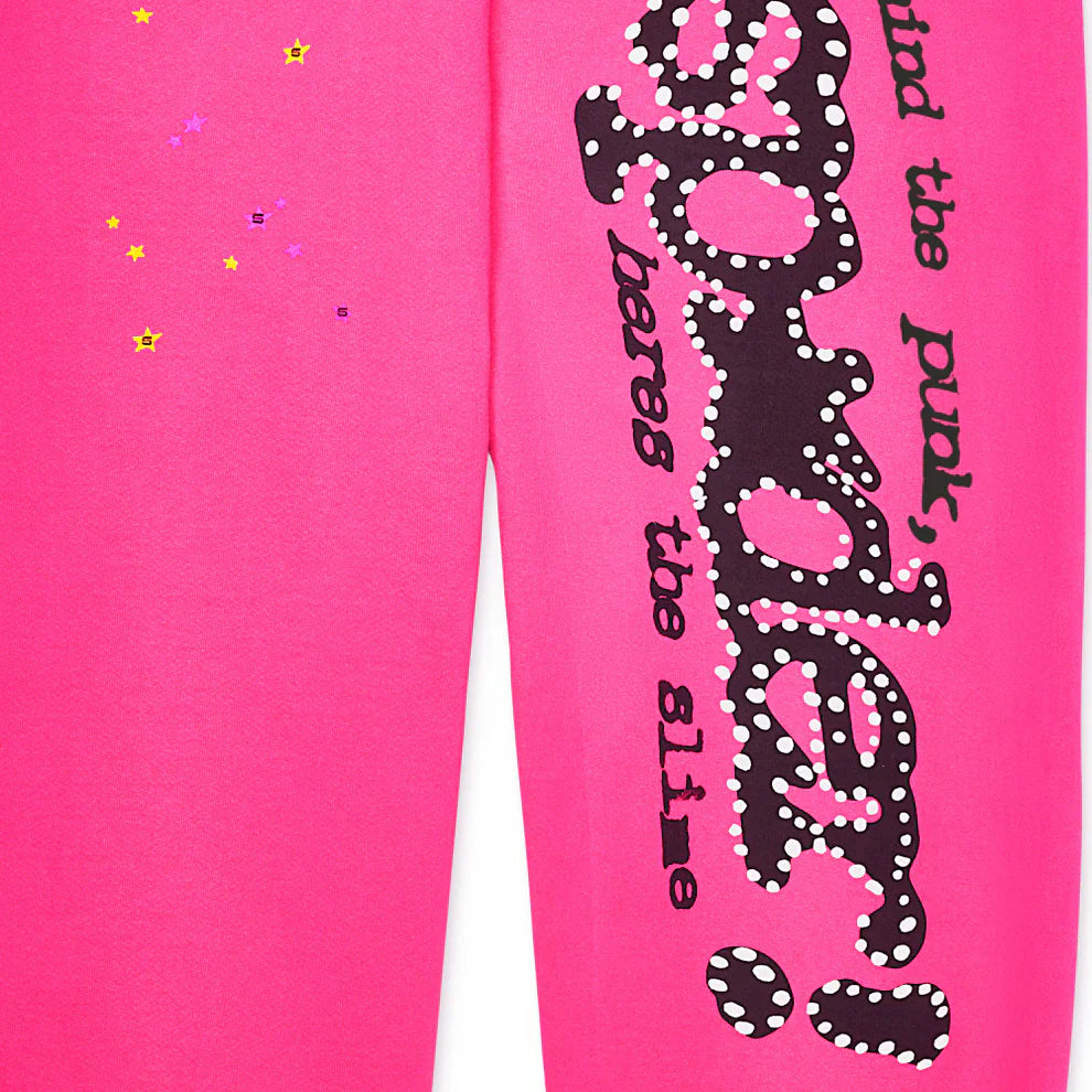Close-up of Sp5der Sweatpants—unisex pink cotton wide leg pants featuring a bold black graphic logo print with white dots, plus scattered yellow and purple star stickers for a vibrant streetwear look.