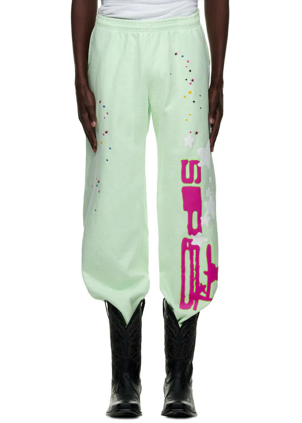 Person wears 100% Cotton Sp5der Sweatpants—Unisex Mint Green Jogger Pants with vertical logo and star graphics, relaxed fit—paired with black cowboy boots and a white top, highlighting a streetwear look focused on the pants.