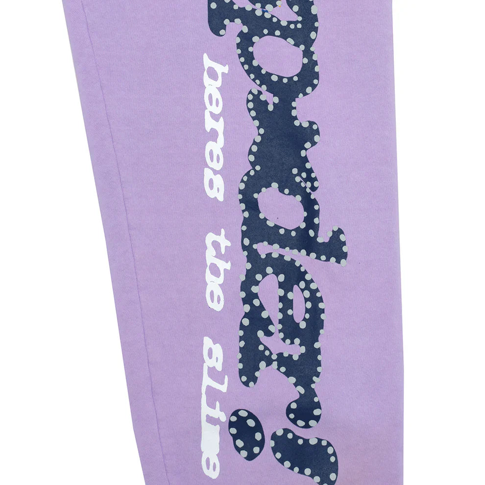 The 100% Cotton Sp5der Sweatpants are unisex lavender jogger pants featuring a vertical logo with star details and a relaxed fit, perfect for streetwear.