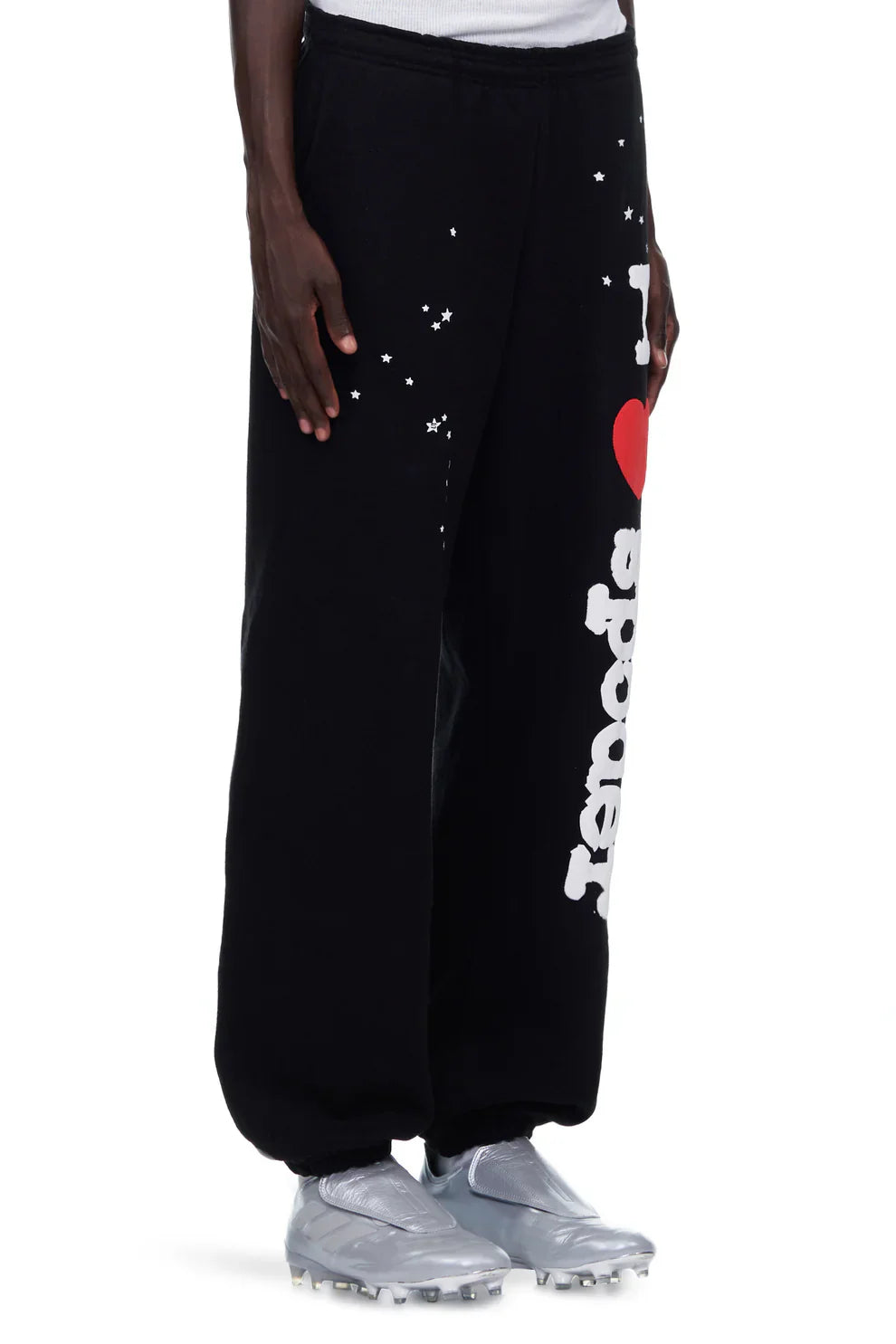 A person wearing unisex 100% Cotton Sp5der Sweatpants—black jogger pants with a bold “I Love Sp5der” graphic and relaxed fit—paired with silver athletic shoes and a white shirt. Only the lower body is shown.