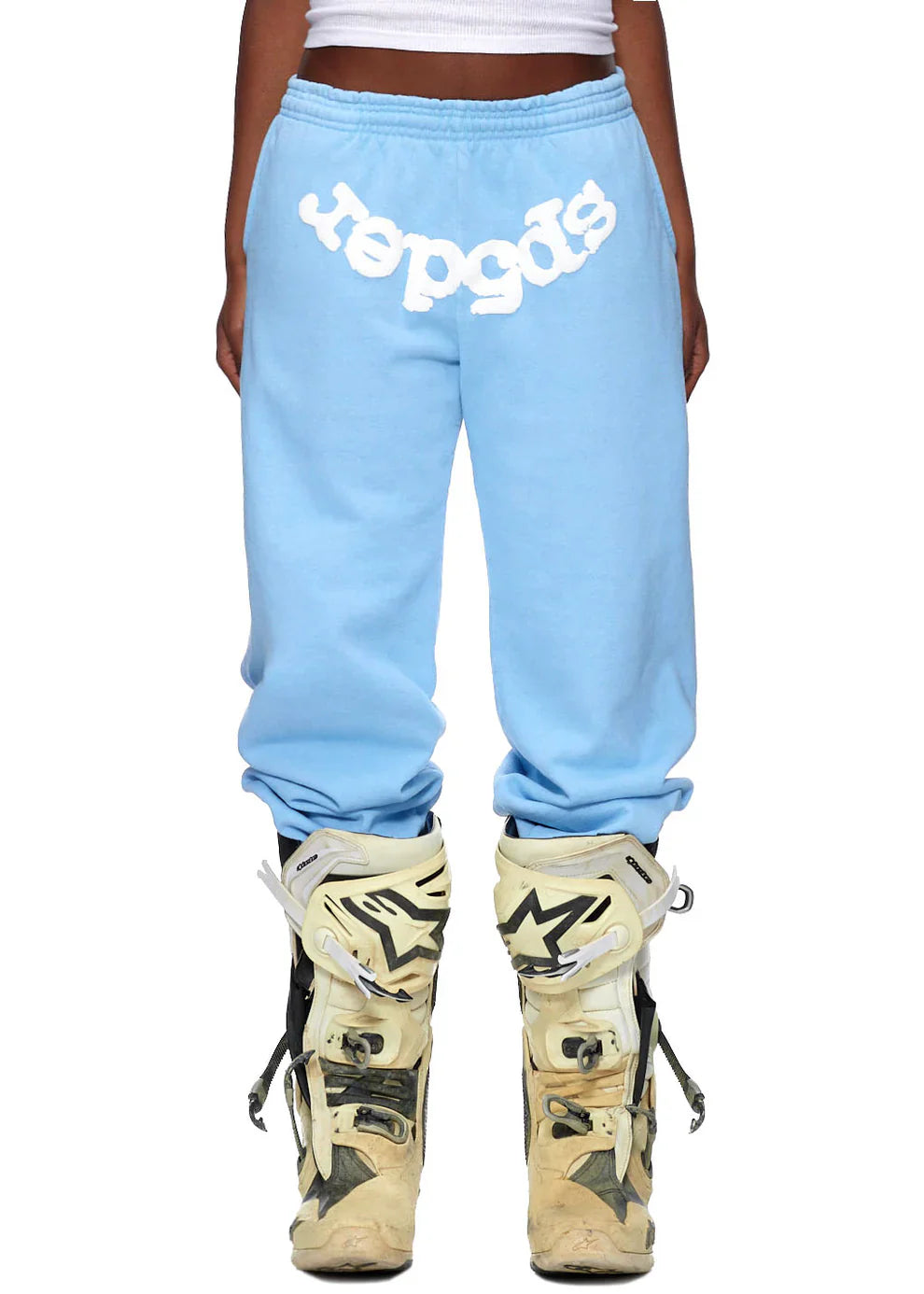 Someone wears Sp5der Sweatpants—unisex light blue cotton sweatpants with a front logo print—styling the streetwear look with oversized, worn beige motocross boots.