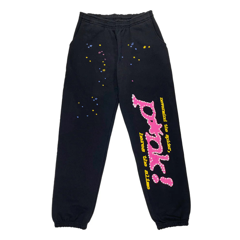 The 100% Cotton Sp5der Sweatpants are unisex black jogger pants with a relaxed fit, featuring colorful star patterns and bold pink logo graphics, combining playful streetwear style with standout details.