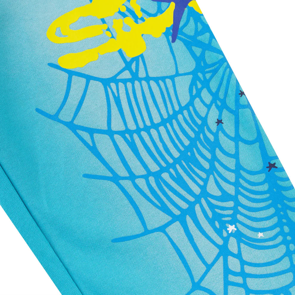 Close-up of 100% Cotton Sp5der Sweatpants—Unisex Blue Jogger Pants with a spider web graphic in darker blue, star accents, and bold yellow and purple shapes. Relaxed fit, perfect for streetwear style.