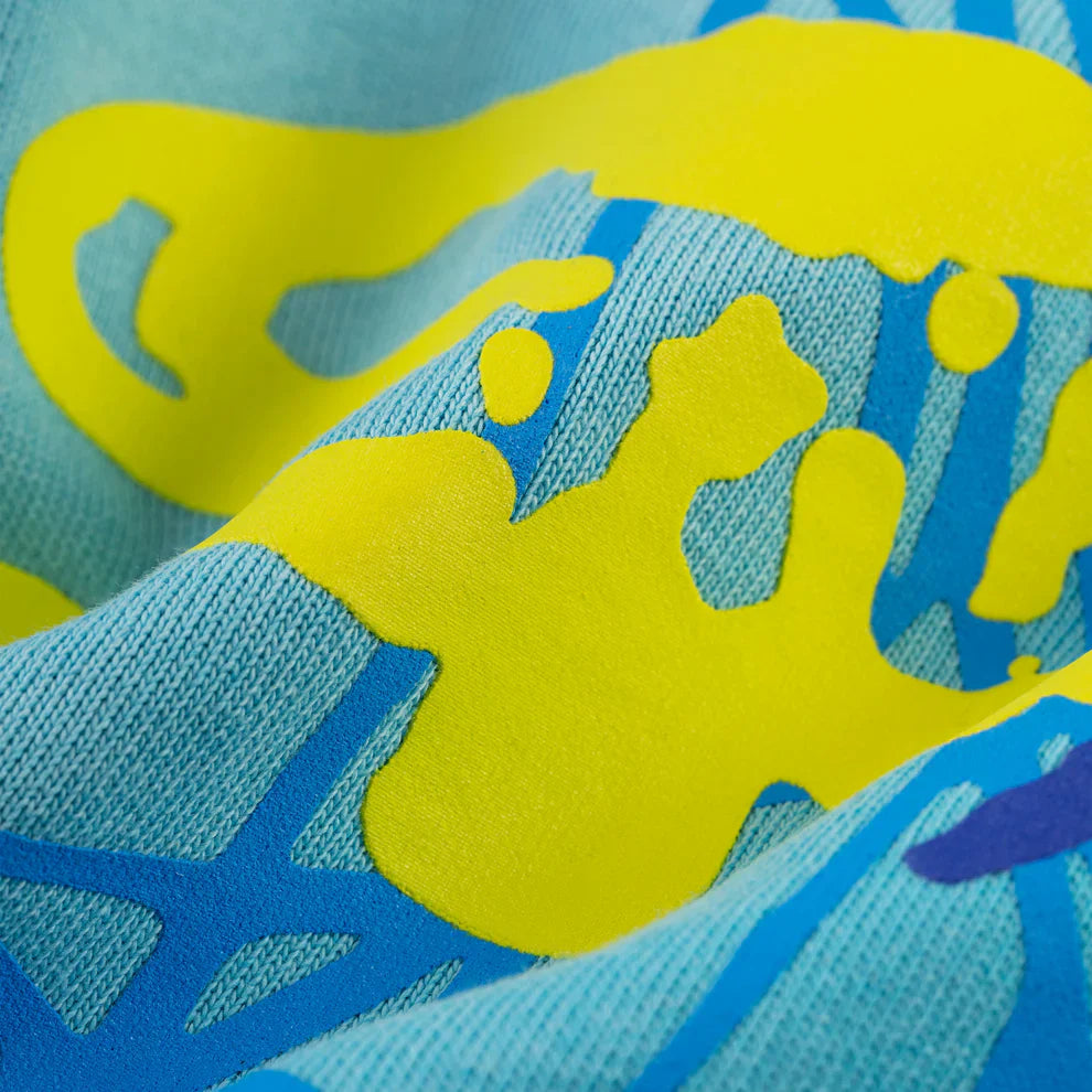 Close-up of 100% Cotton Sp5der Sweatpants—unisex blue jogger pants with spider web graphics and star details. The knit texture and raised print accents highlight the relaxed fit and streetwear style.