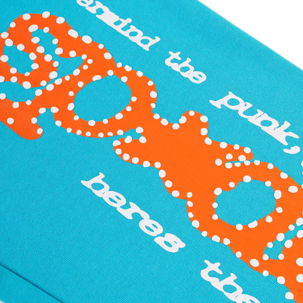 Close-up of 100% Cotton Sp5der Sweatpants—Unisex Teal Jogger Pants with an orange logo print and relaxed fit. Features partial white text on blue fabric, streetwear-inspired.