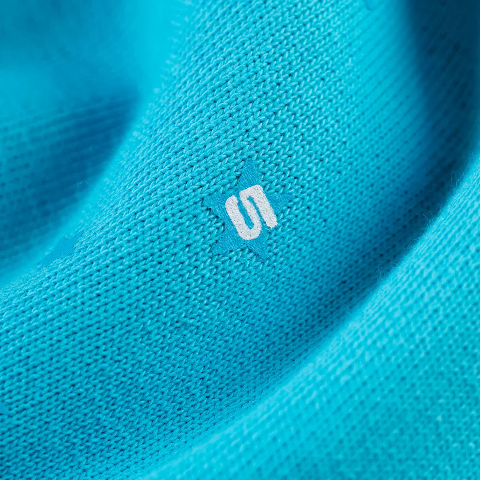 Close-up of textured teal 100% cotton Sp5der Sweatpants—unisex jogger pants with a relaxed fit and an orange geometric logo print, highlighting the visible weave pattern and threads of this streetwear material.