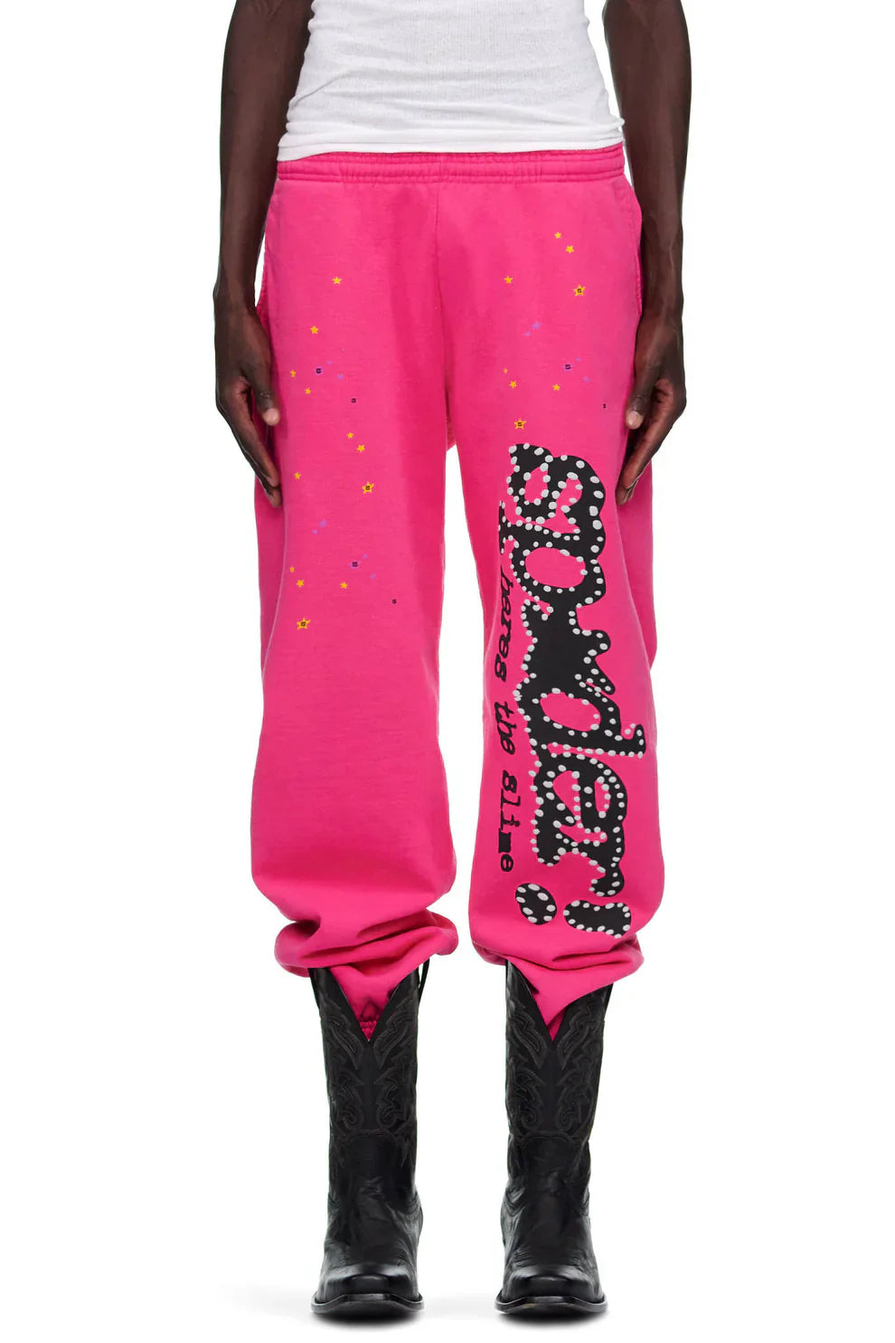 A person wearing Sp5der Unisex Pink Cotton Wide Leg Sweatpants with a graphic logo print, styled with black cowboy boots and a white shirt.