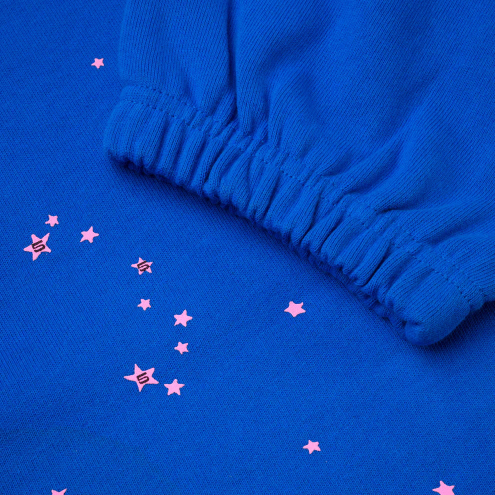 A close-up of 100% Cotton Sp5der Sweatpants—unisex blue joggers with a pink logo and star accents, elasticated cuffs, and a relaxed fit, perfect for streetwear.