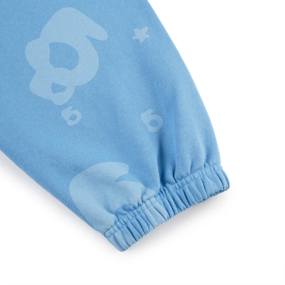 A close-up of the Sp5der Light Blue All-Over Print Sweatpants, crafted from 100% cotton, with elastic cuffs and playful abstract animal faces and numbers in a lighter blue—a unisex streetwear jogger style.