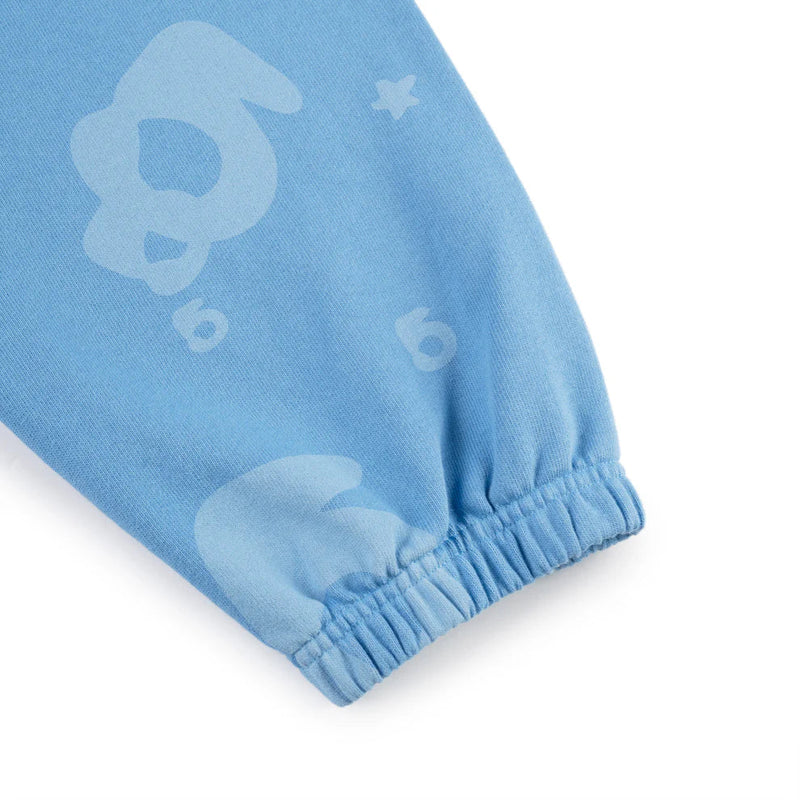 A close-up of the Sp5der Light Blue All-Over Print Sweatpants, crafted from 100% cotton, with elastic cuffs and playful abstract animal faces and numbers in a lighter blue—a unisex streetwear jogger style.