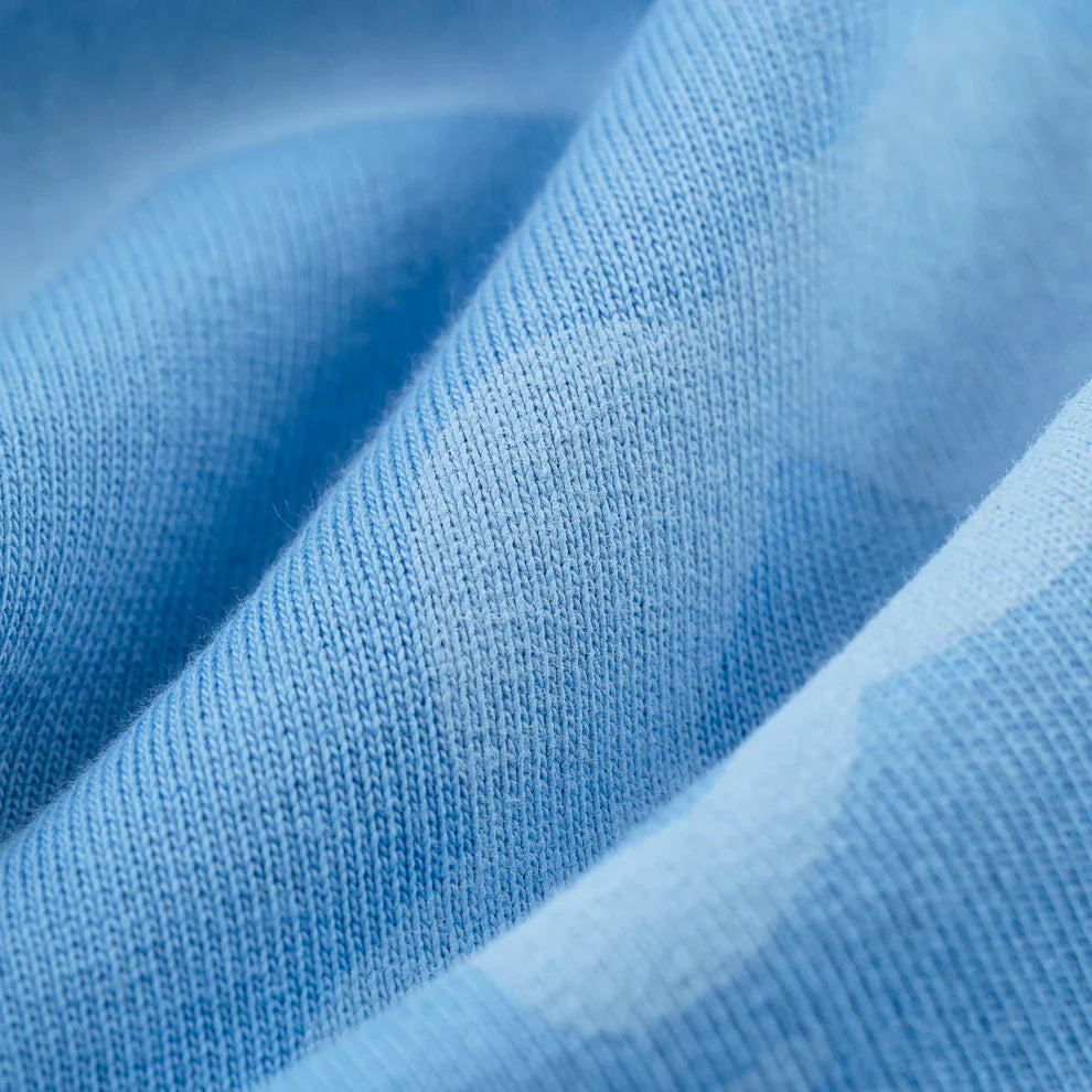 Close-up of light blue fabric with visible knit texture and soft folds, made from 100% premium cotton—perfect for Sp5der Light Blue All-Over Print Sweatpants, stylish unisex streetwear joggers.