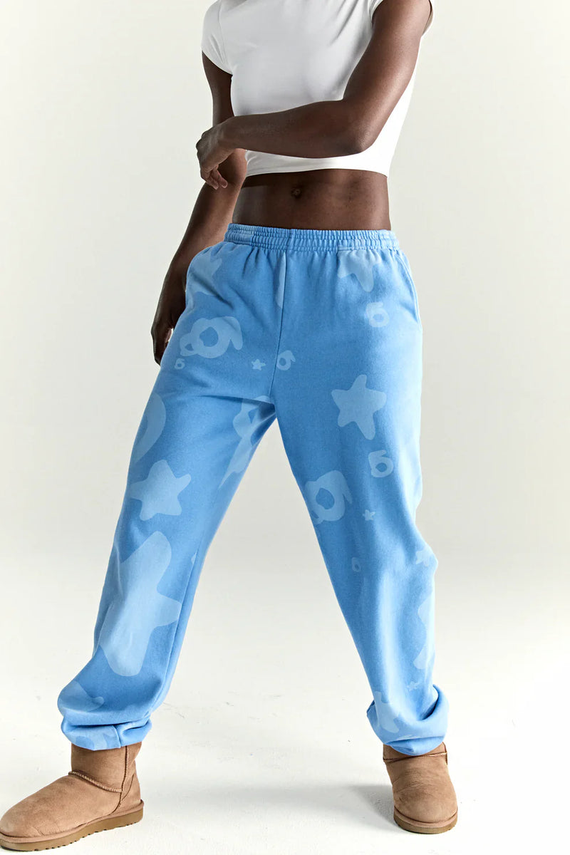 A person in a white crop top, Sp5der Light Blue All-Over Print Sweatpants 100% Cotton Unisex Streetwear Joggers, and tan UGG-style boots stands against a plain light background.