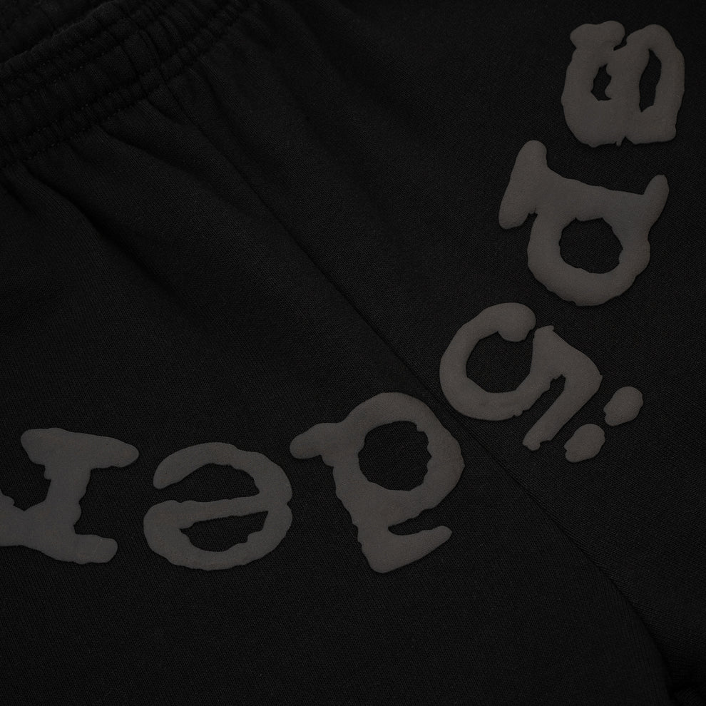 Close-up of Sp5der Black Tonal Logo Sweatpants—100% cotton unisex streetwear joggers—showing grey, raised, stylized letters near the elastic waistband for distinctive style.