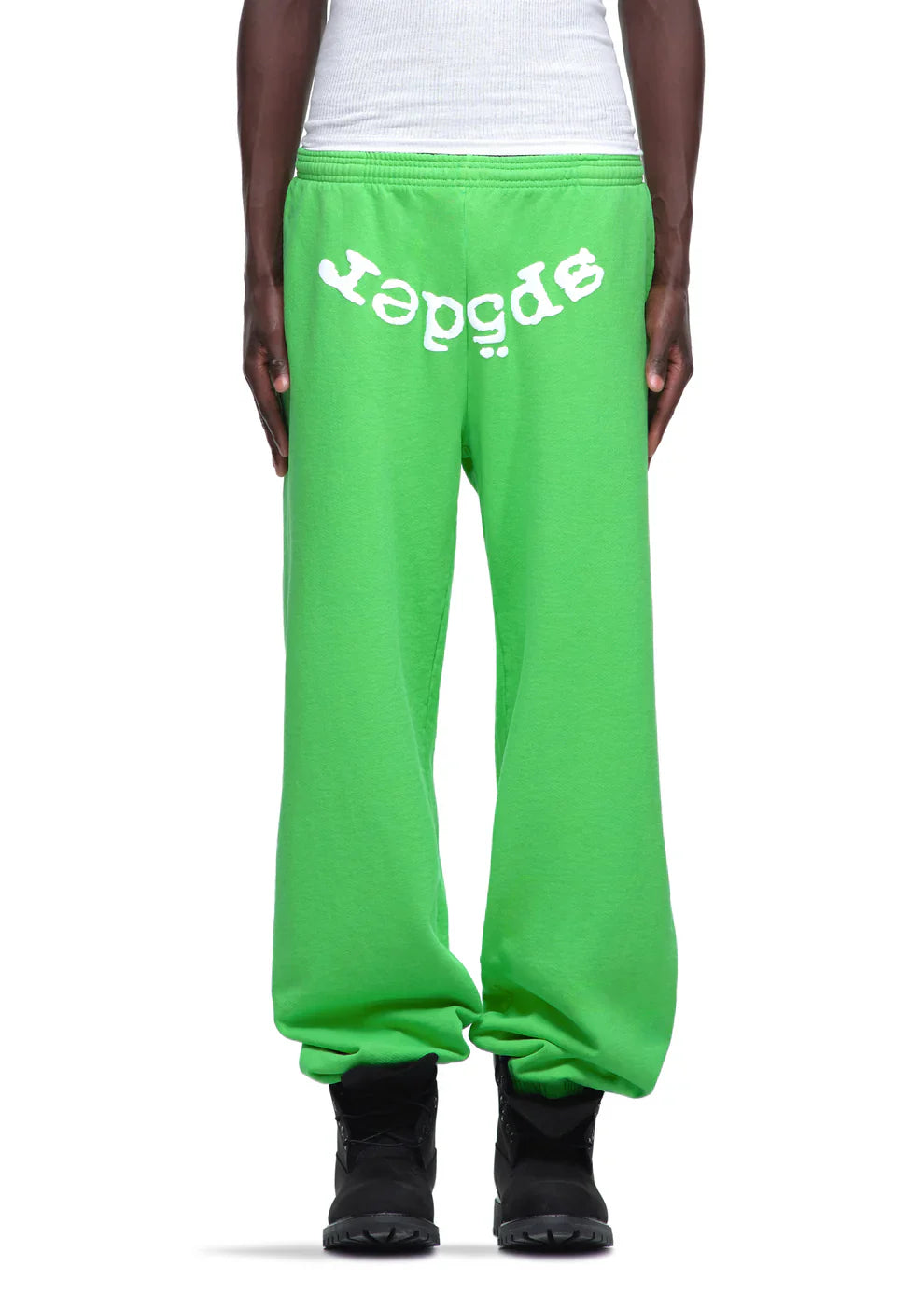 Someone wears unisex Sp5der Sweatpants—green cotton joggers with a front logo print—paired with a white shirt and black shoes for an eye-catching, streetwear-inspired look.