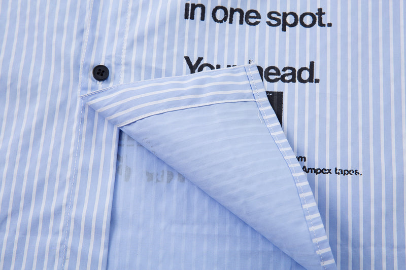 Front hem flap detail on a light blue pinstripe shirt with black printed text behind