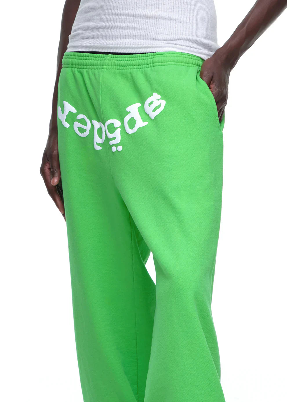 Wearing Sp5der Sweatpants – Unisex Green Cotton Sweatpants with a front logo print, paired with a white ribbed tank top, this look redefines green streetwear through bold style and all-day comfort.