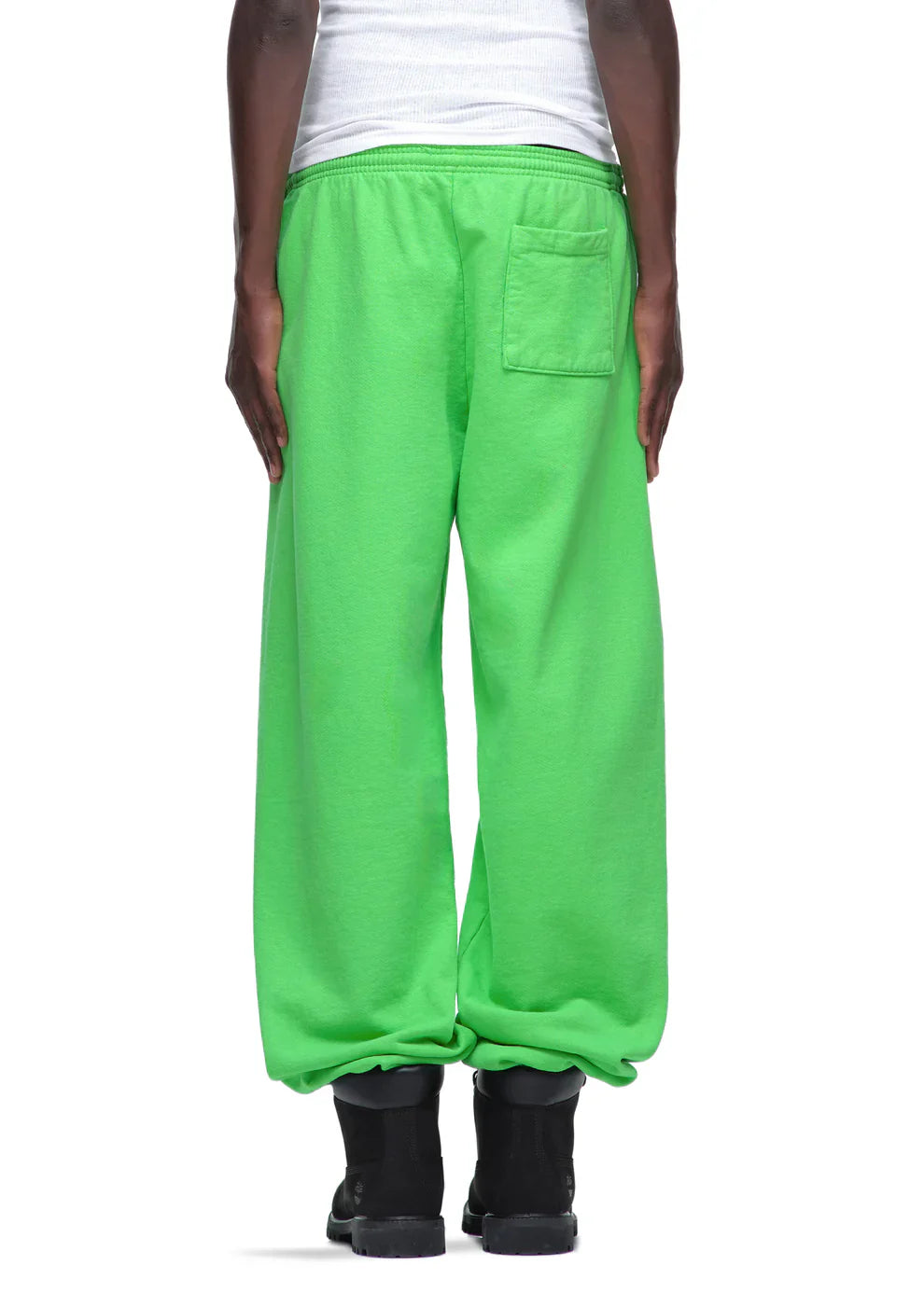 A person wearing loose-fitting Sp5der Sweatpants – unisex green cotton sweatpants with front logo print, styled with black boots and a white shirt, shown from behind on a white background for a bold streetwear look.
