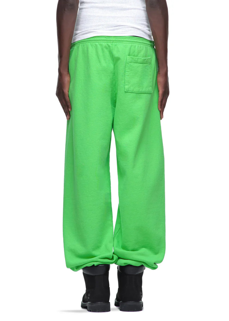 A person wearing loose-fitting Sp5der Sweatpants – unisex green cotton sweatpants with front logo print, styled with black boots and a white shirt, shown from behind on a white background for a bold streetwear look.