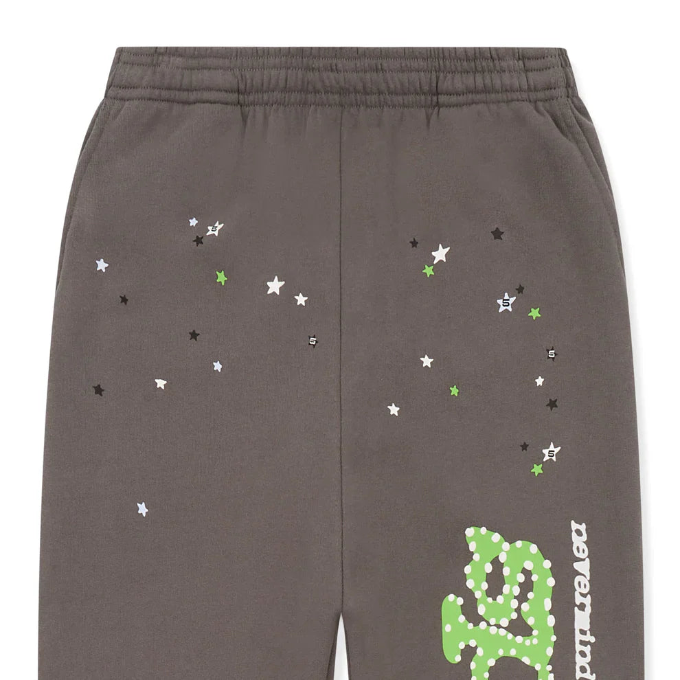 The Sp5der Sweatpants are unisex dark grey cotton joggers featuring an elastic waistband, a green logo on the side, and scattered white, green, and black star prints for a standout streetwear style.