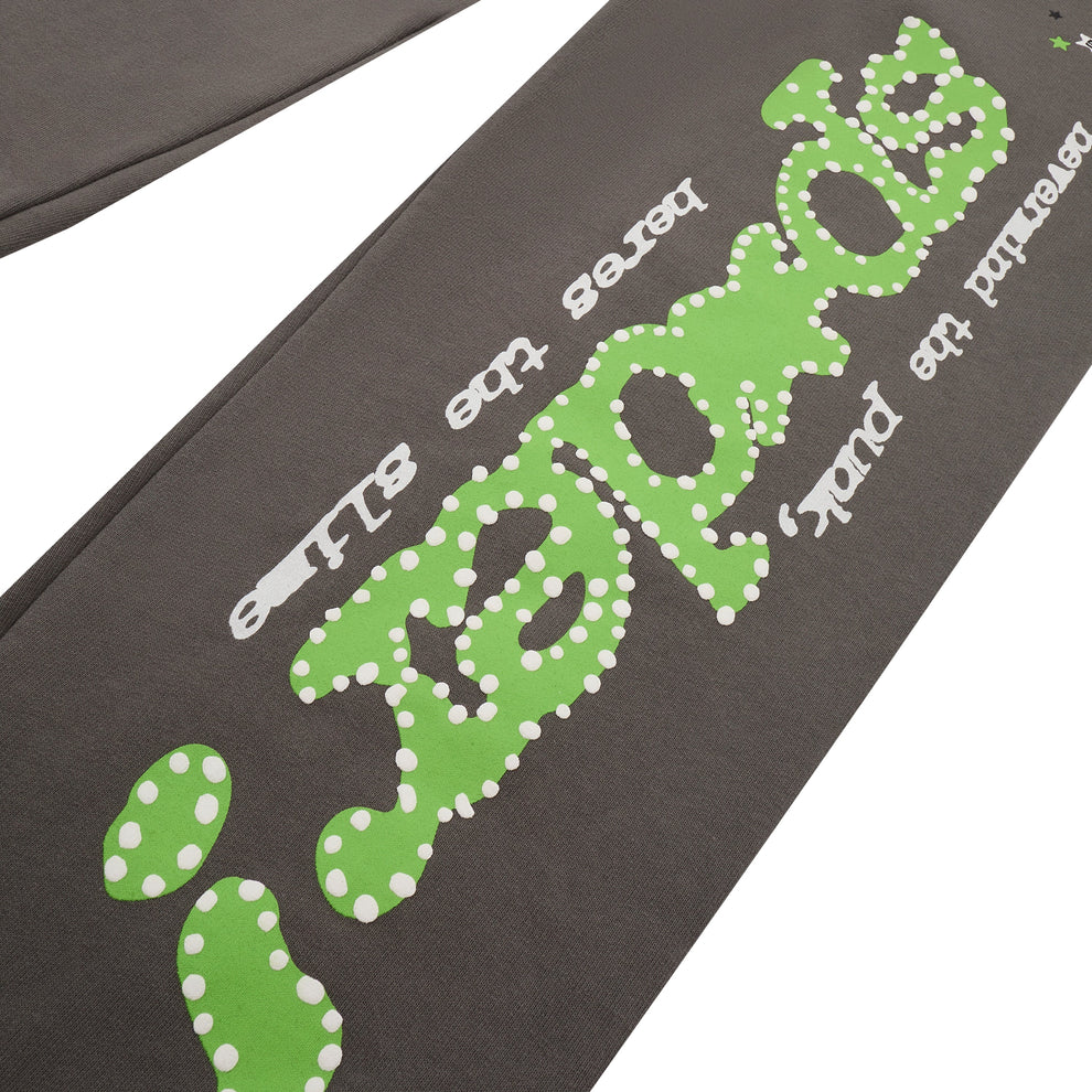 Close-up of Sp5der Sweatpants: unisex dark grey cotton with a green side logo and star print, featuring playful, graphic text in an irregular font—perfect for adding a fresh streetwear vibe.