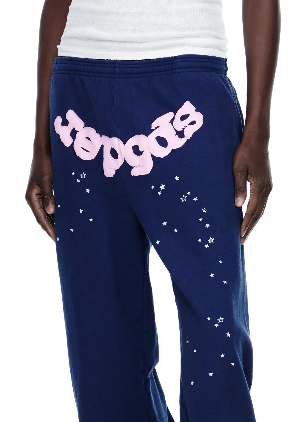 A person wears Sp5der Sweatpants – unisex navy blue cotton sweatpants featuring a pink front logo and white star print, stylish and comfortable for streetwear.