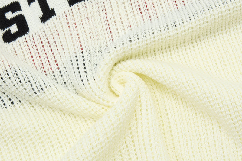 Close-up of a cream varsity knit polo with black lettering and textured mesh fabric in a soft spiral fold