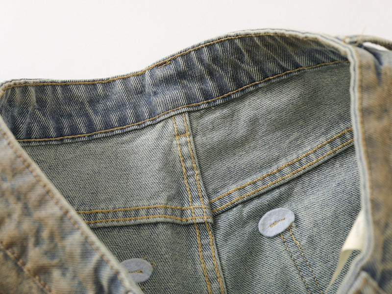 Close-up inside the waistband of faded blue denim pants showing stitching and button closure details