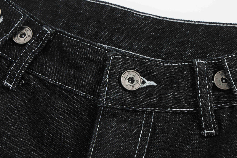 Waistband detail of black denim shorts with silver button fly and white stitching