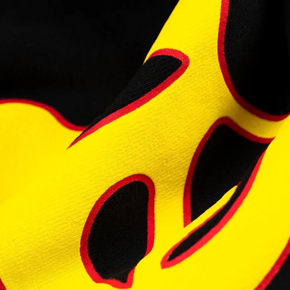 A close-up of the Sp5der Sweatpants – Unisex Black Cotton Sweatpants, highlighting the vibrant yellow flame side logo outlined in red and star print that showcase its bold colors and unique texture.