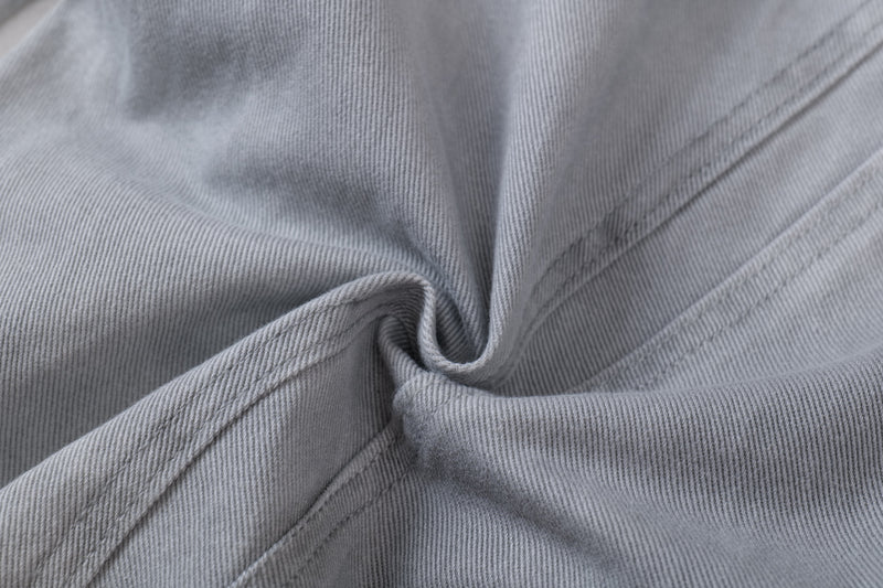 Close-up of light gray denim fabric and seam intersection with folded sculptural drape