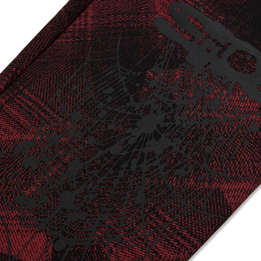 A close-up of Sp5der Sweatpants – Unisex Red and Black Patterned Cotton Sweatpants with graphic detail, featuring a black spider web design and bold black text.