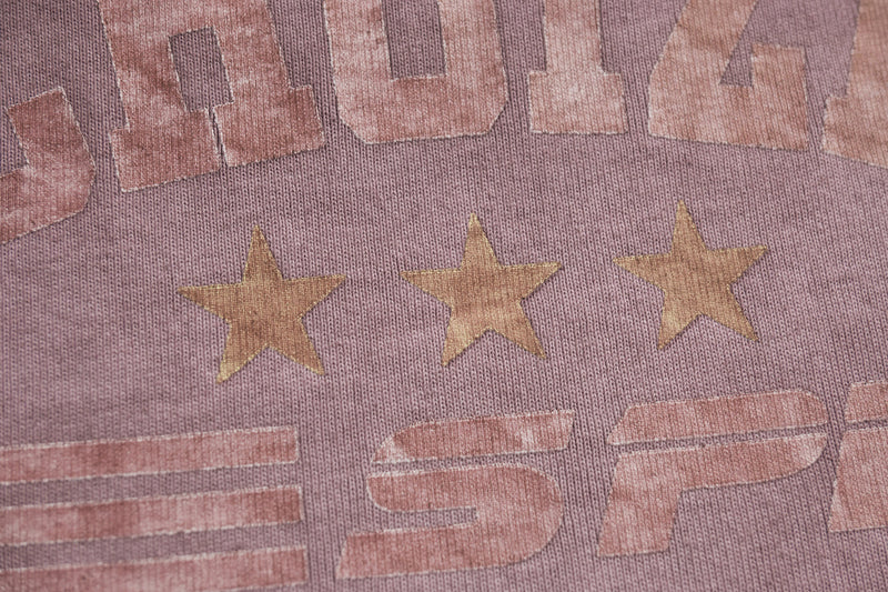 Close-up of a vintage wash racing graphic tee with faded stars and retro text on dusty pink fabric