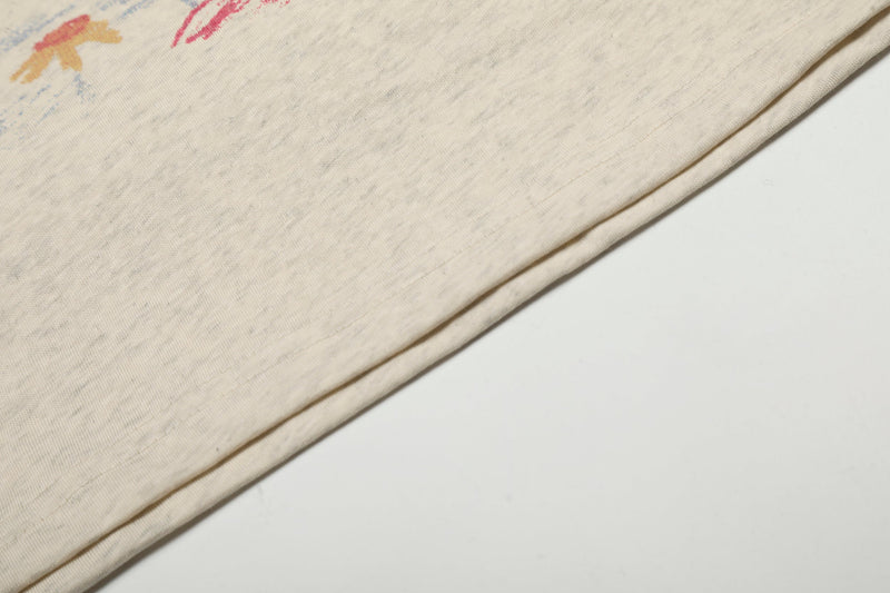 Folded cream tee with partial multicolor print visible near the edge