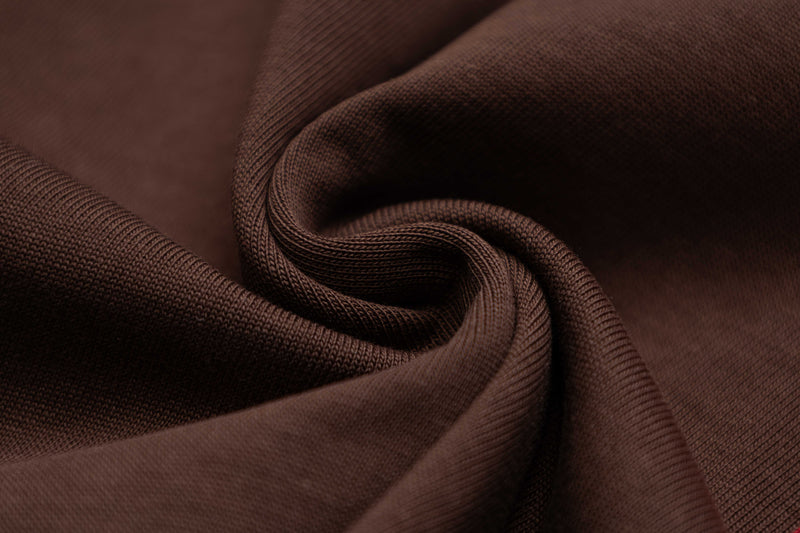 Close-up of rich brown textured knit fabric with soft folds, showcasing the oversized retro sportswear tee material