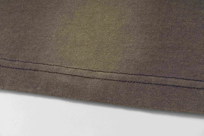 Close-up of a washed brown abstract sketch tee hem with visible double stitching and vintage worn texture