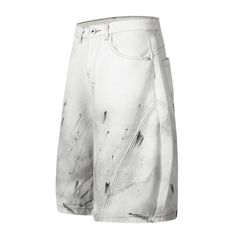 Three-quarter front view of white wide-leg denim shorts with black paint splatter and side seam details