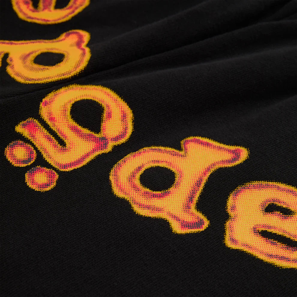 Close-up of Sp5der Sweatpants—unisex black cotton fabric with bold, distorted yellow letters outlined in red, resembling a flame logo. The partial lettering adds urban flair and playful style to this vibrant design.