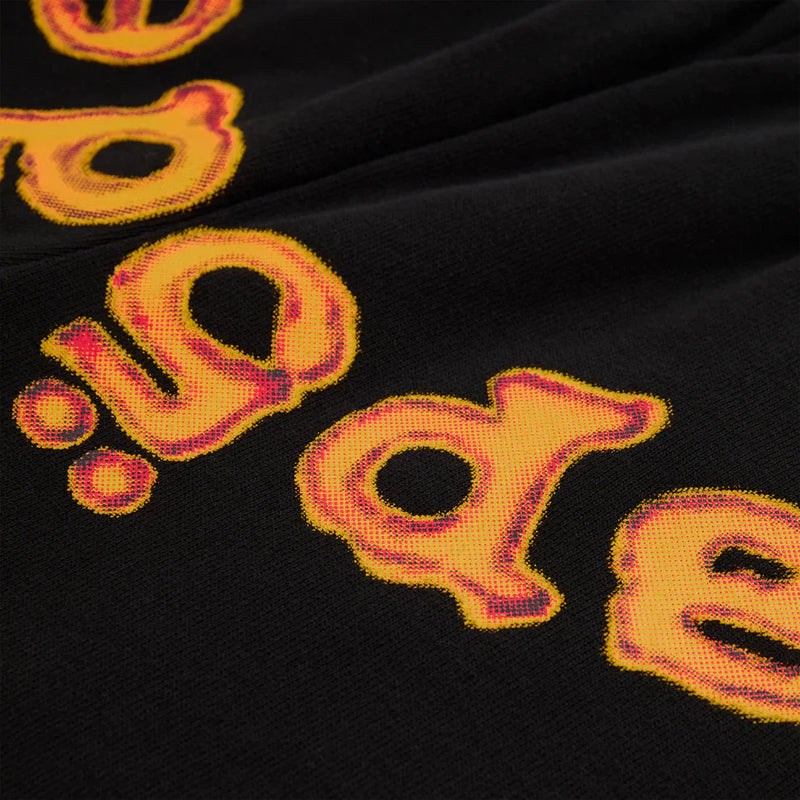 Close-up of Sp5der Sweatpants—unisex black cotton fabric with bold, distorted yellow letters outlined in red, resembling a flame logo. The partial lettering adds urban flair and playful style to this vibrant design.