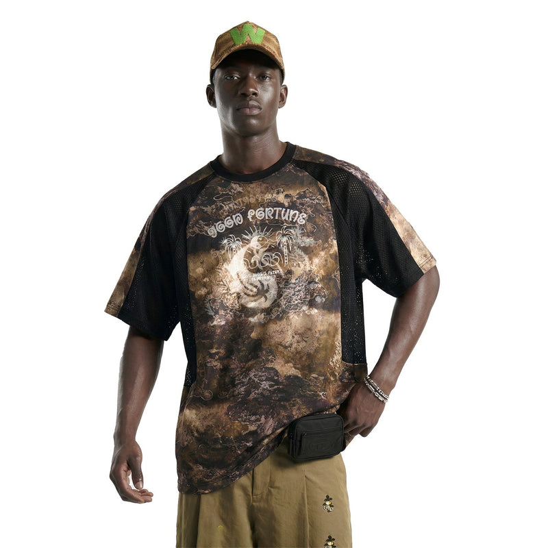 Model wearing a desert fortune graphic mesh performance tee with black mesh sleeves, camo cap, and khaki shorts on white background