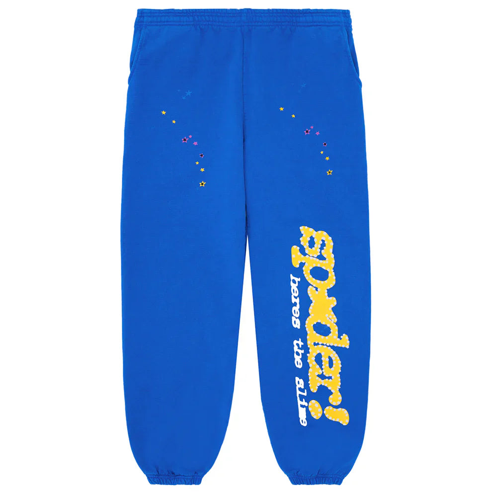 The Sp5der Sweatpants are unisex blue cotton joggers with an elastic waistband, yellow side logo, and multicolored star print near the pockets—bold statement streetwear perfect for anyone.