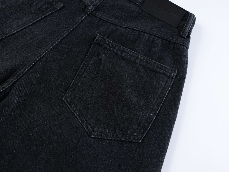 Back pocket detail on black denim shorts with curved seam and logo patch at waistband