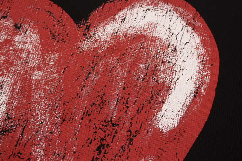 Close-up of a distressed red heart graphic on black streetwear tee with a grunge, melted paint texture