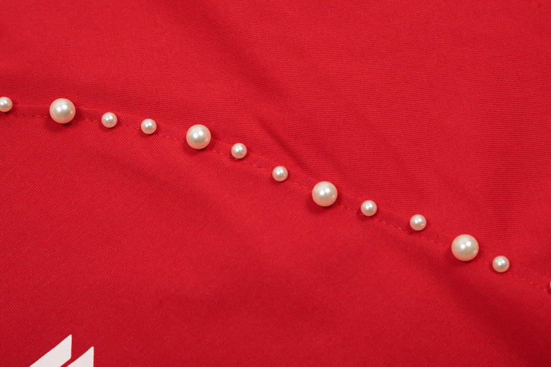 Close-up of a red studded raglan cotton tee with pearl-like accents and visible seam detail