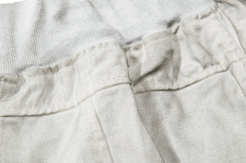 Close-up of front seam and textured paneling on light gray denim shorts