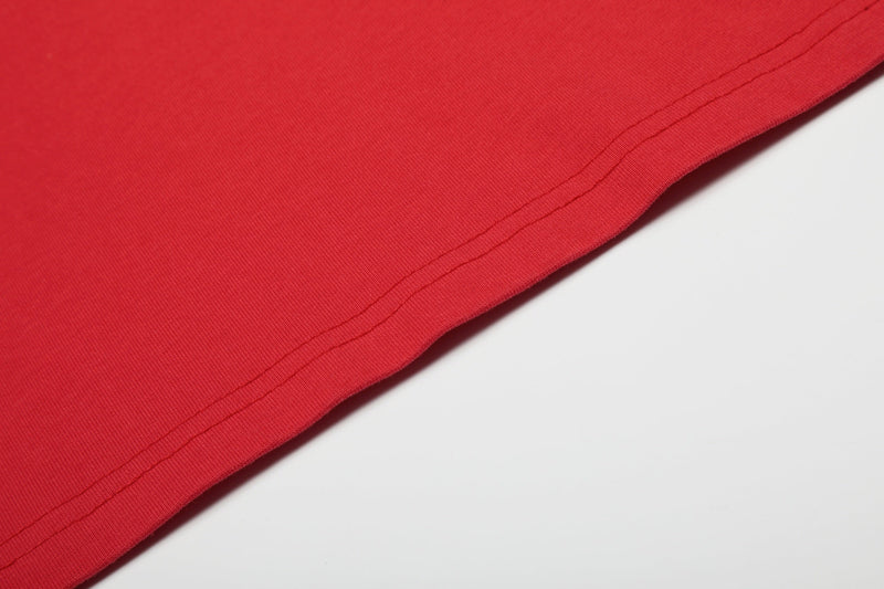 Close-up of a red vintage distressed graphic tee hem with visible stitching on a white background