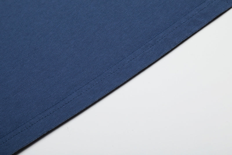 Close-up of blue washed cotton tee hem with visible stitching and soft faded texture